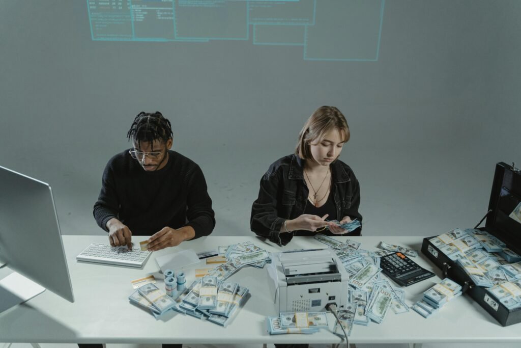 Two people counting money at a desk with computers and cash equipment.